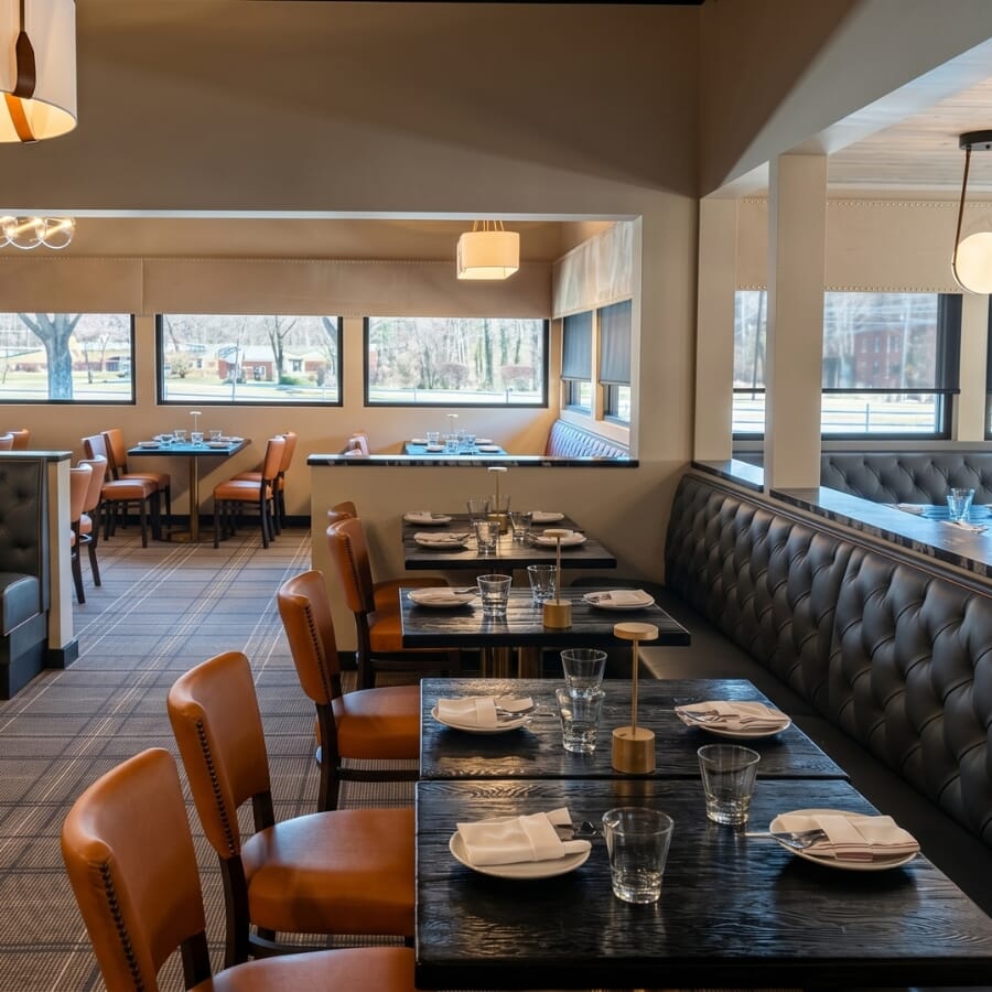 Restaurant dining area with claret tufted booth seating, saffron upholstered chairs, black tables, gold bases, mirrors, and decorative lighting.