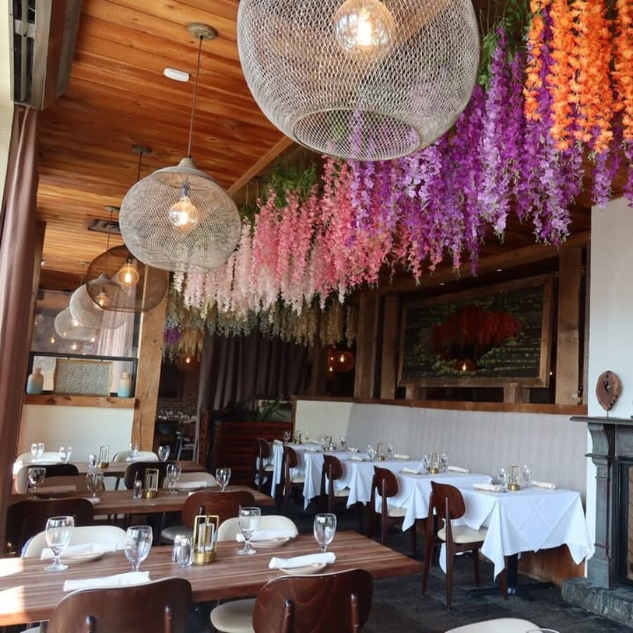 Dining room at Bora Restaurant with cream upholstered chairs, walnut wood tables, floral ceiling décor, and large windows.