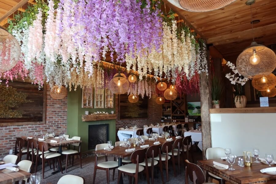 Warm bar and dining atmosphere at Bora Restaurant in Bethel Connecticut featuring wood ceilings, floral décor, pendant lighting, and commercial restaurant seating.