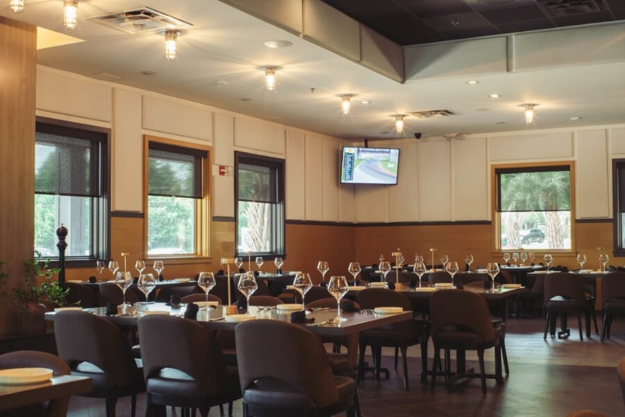 Italian Chophouse on Lake Oconee group dining room with custom upholstered commercial chairs, high-back accent seating, wood tables, wine glasses, and black furniture.