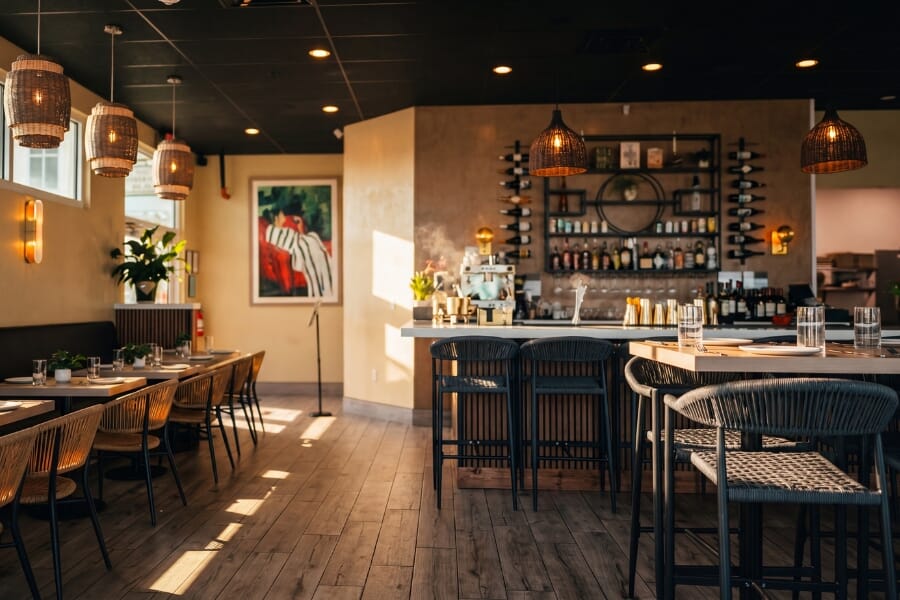 The Whistling Duck wine and charcuterie bar in Surfside Beach featuring coastal restaurant furniture, rope chairs, oak table tops, black table bases, gray bar stools, and upholstered booth seating.