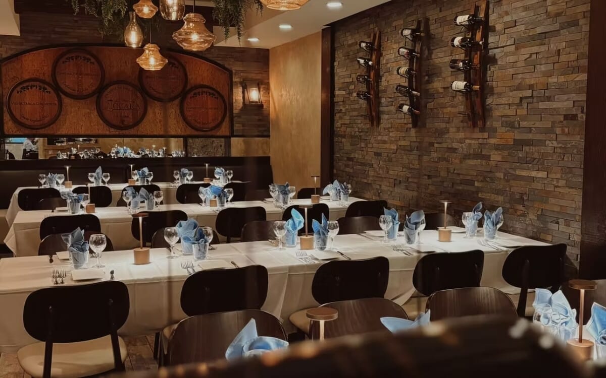 Main dining room at Villaggio Iccara in Hamilton Township, New Jersey featuring white stone tables, walnut dining chairs, and warm lighting.