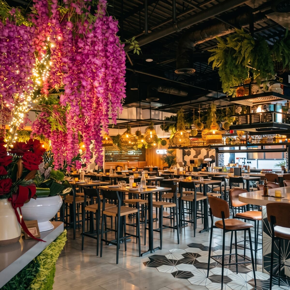 Vida bar-height seating with tan rope-seat stools, dark frames, pendant lights, and a purple floral display.